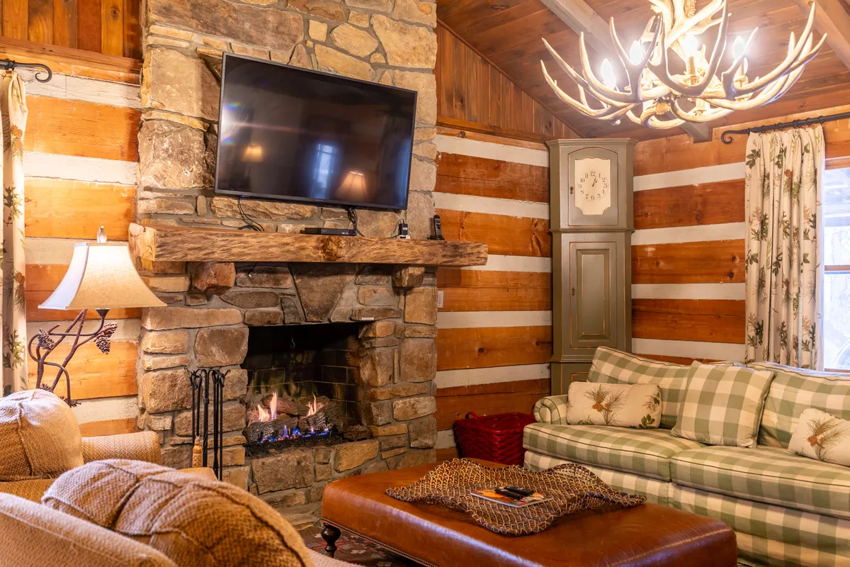 A plush living area with a stone fireplace, plaid sofa, wooden beams, and a visible HD Smart TV. The room glows with warmth and offers a cozy retreat for relaxing, watching movies, or gathering around the fire after a day of adventure.
