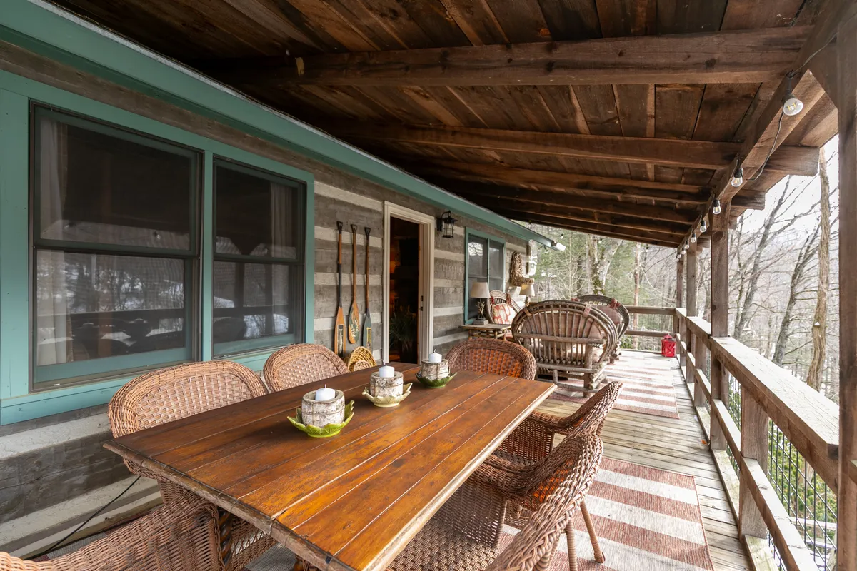 A wooden table surrounded by wicker chairs sits on a porch with natural surroundings and decorative lanterns, offering a comfortable and cozy atmosphere for outdoor dining or special gatherings. The setting is ideal for enjoying meals together or celebrating occasions while connected to the beauty of the outdoors.