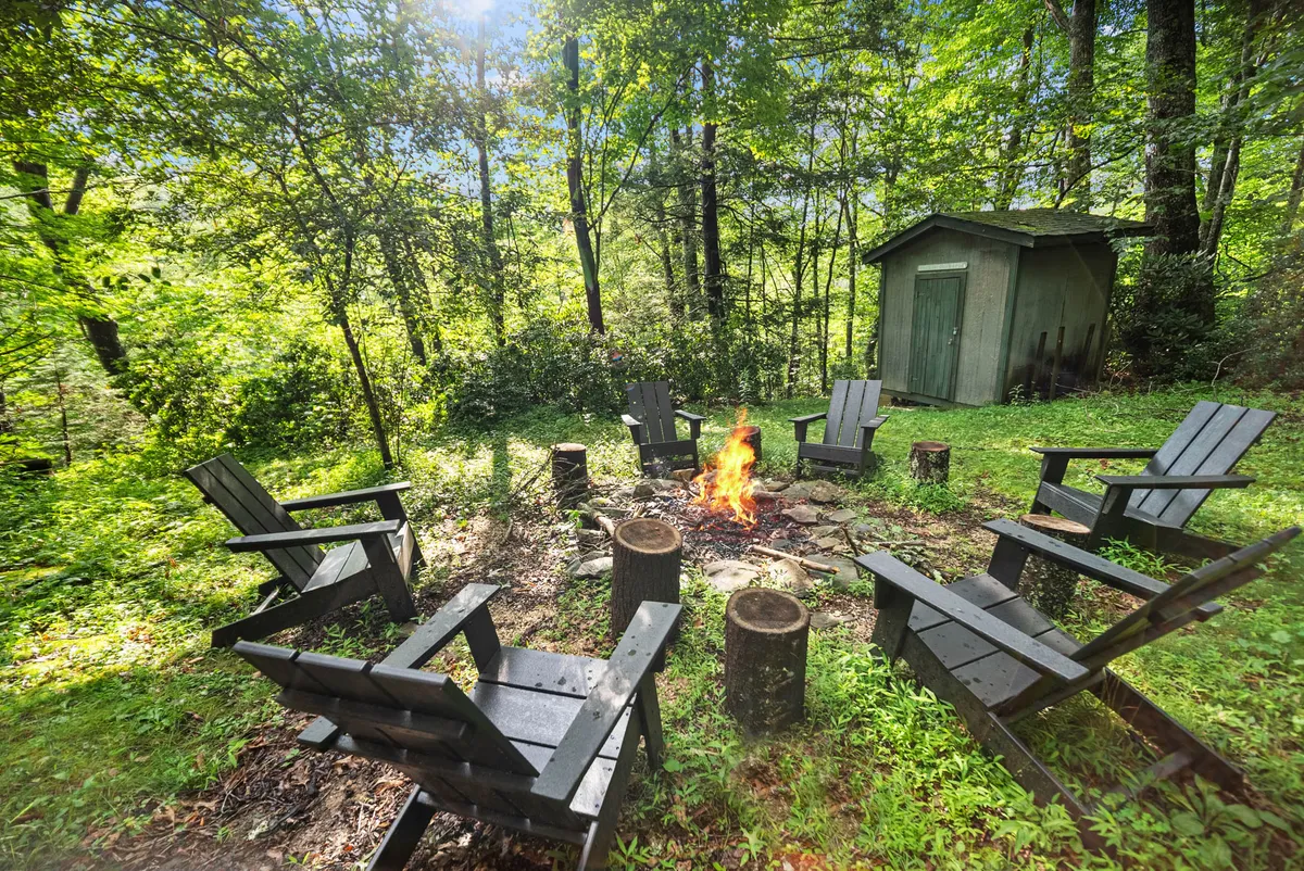 A cozy fire pit area surrounded by chairs, set against greenery and a shed, providing a perfect outdoor gathering spot for storytelling, roasting marshmallows, or stargazing as a family.