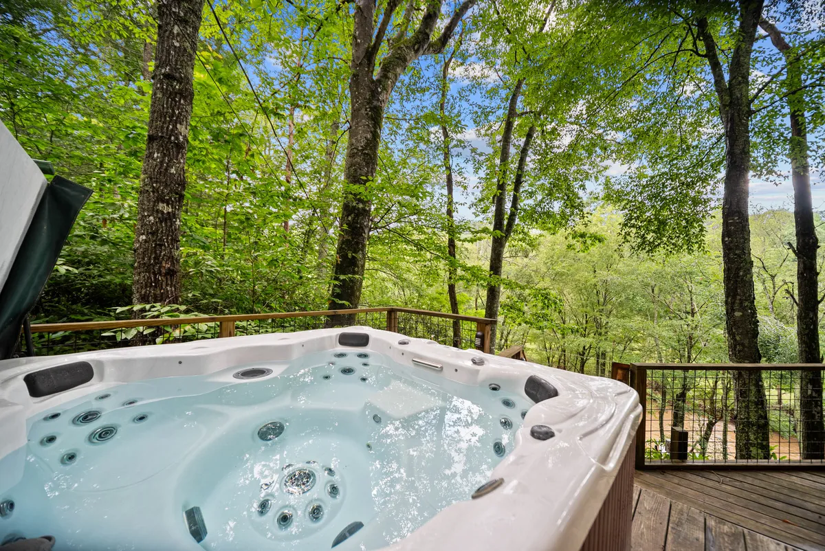 A bubbling hot tub nestled on a wooden deck, enveloped by lush trees and mountain vistas. The intimate setting is ideal for unwinding under the stars or enjoying peaceful solitude surrounded by nature’s sounds.