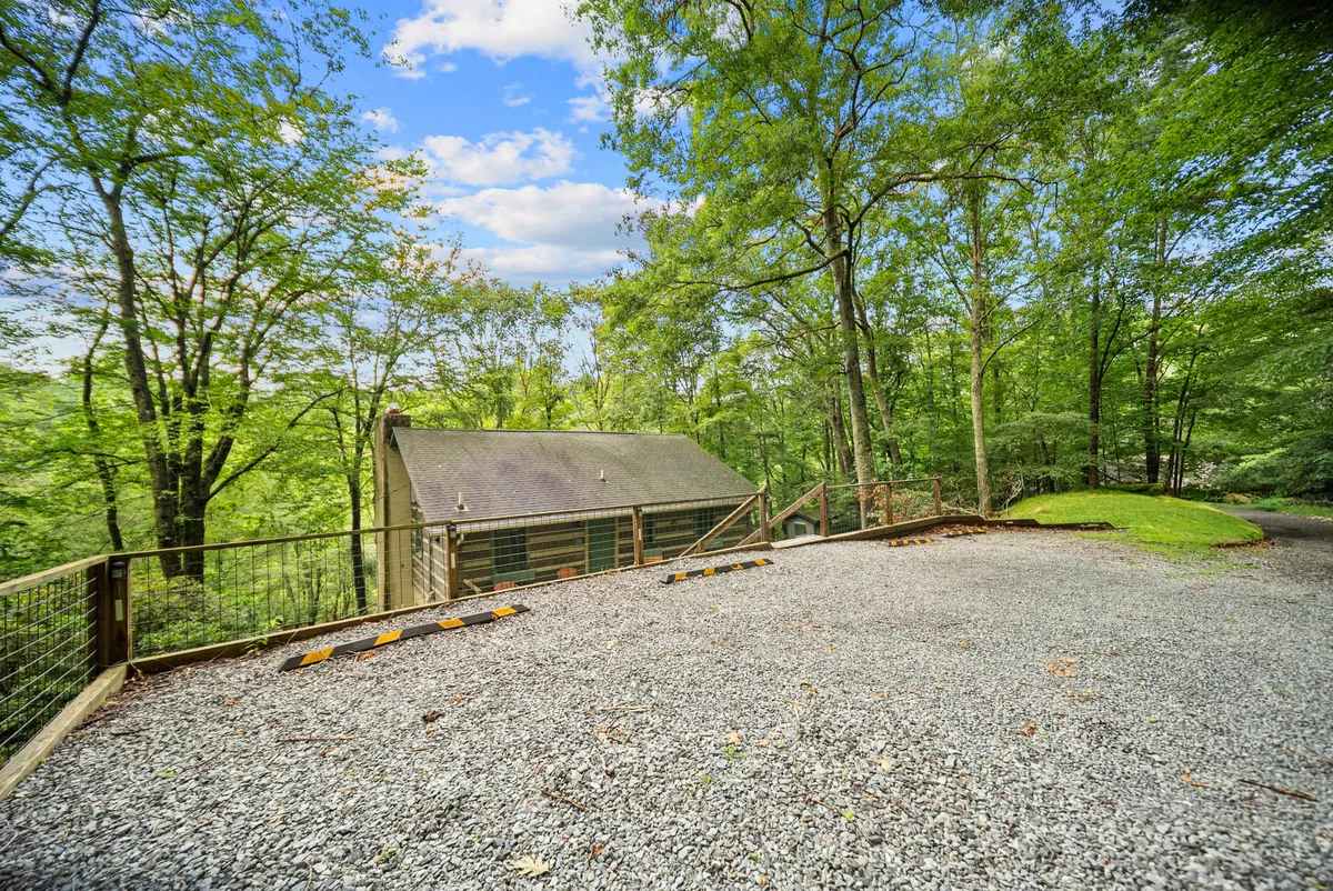 An exterior shot showing a gravel parking area in front of the home, surrounded by trees, seamlessly blending the structure into its natural setting. The ample lot underscores easy access and practical features for families or groups arriving with multiple vehicles.