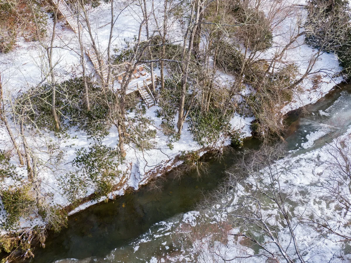 This image features snow-covered riverbanks, glistening water, and wooden steps leading directly down to the river. The serene, natural setting highlights the property's easy and direct access to the water, inviting fishing, floating, or quiet riverside moments.