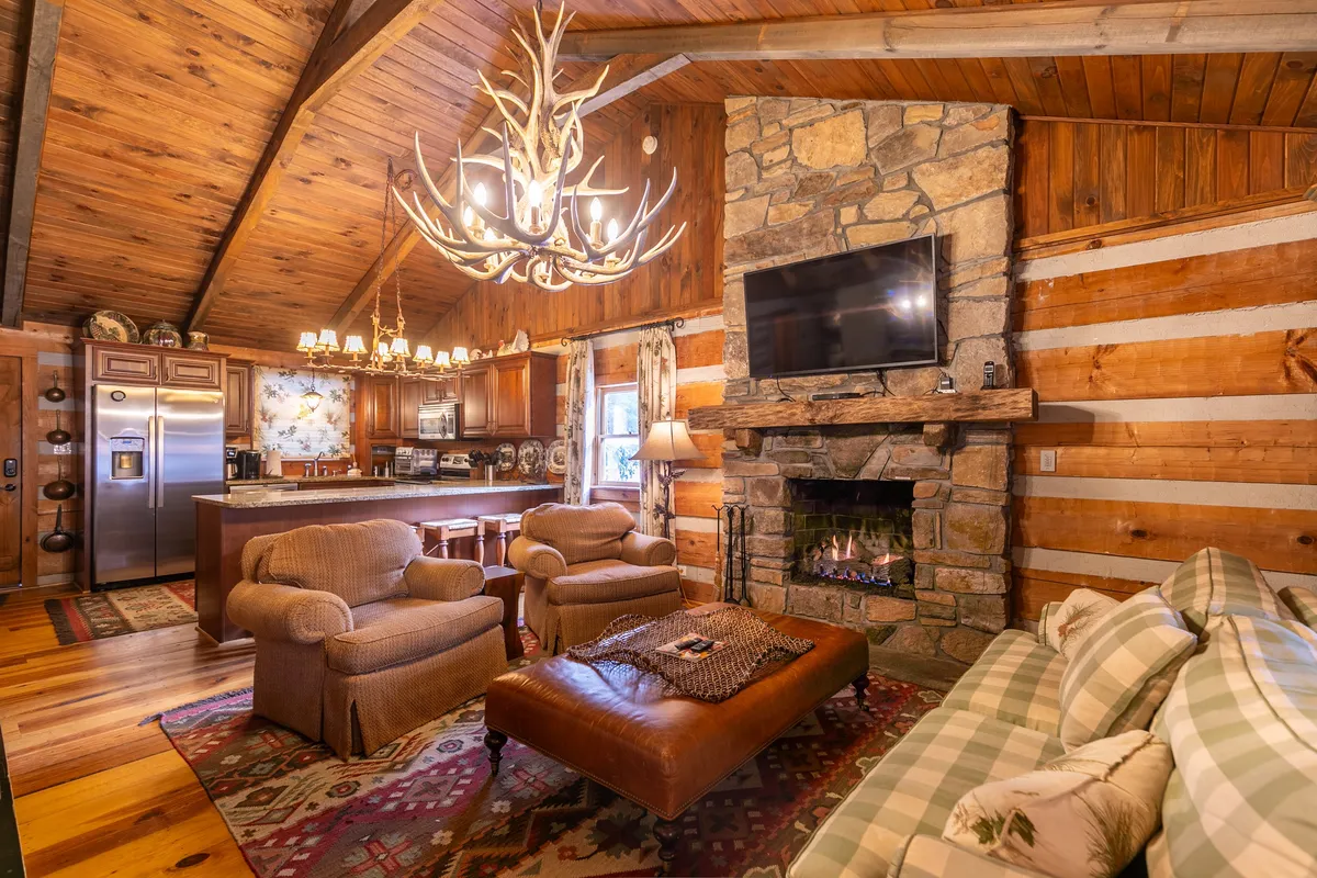 This image features a spacious living area anchored by a stone fireplace, a plush sofa adorned with throw pillows, a dramatic chandelier, and a visible kitchen island. The scene exudes warmth and comfort, ideal for family gatherings and relaxation after a day of mountain adventure.