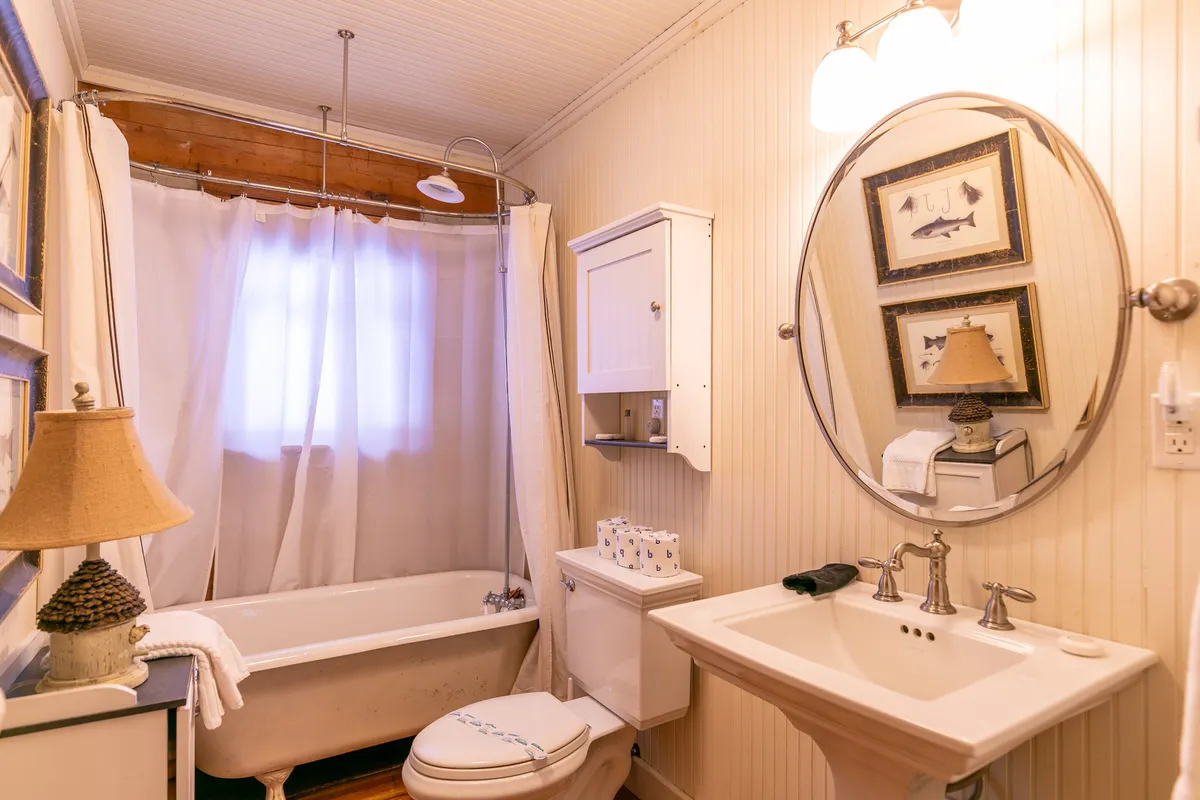 A full bathroom with a spacious bathtub, sink, mirror, lamp, and tasteful wall decor, offering a tranquil setting for relaxation and self-care routines.