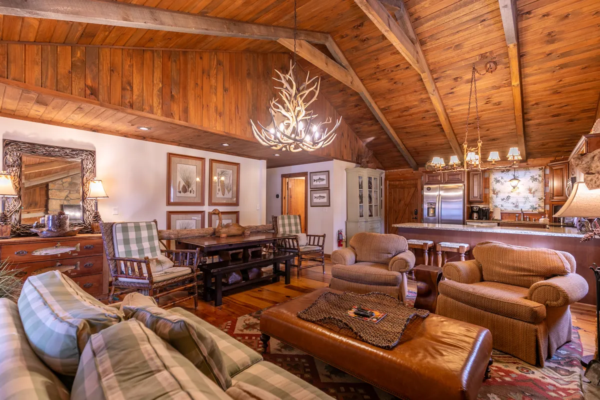 A spacious, warmly lit dining area features a large wooden table under an antler chandelier. Plush seating and a decorative mirror add a sense of comfort and style. The setting invites family and friends to sit together, share meals, and enjoy celebrations.